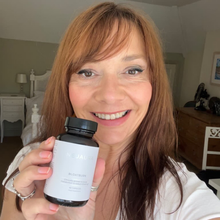 A person smiling and holding a bottle labeled 'Metabolic+' in a bright, well-lit room.