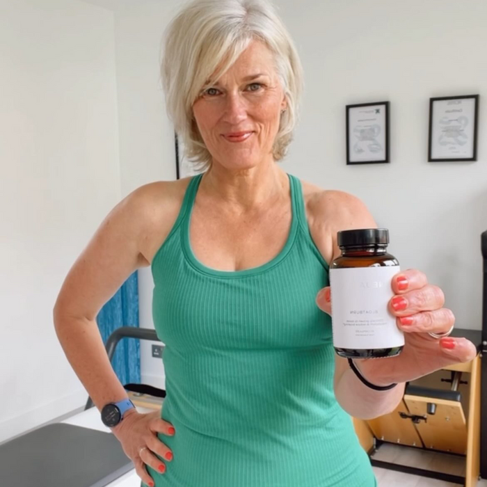 A person smiling and holding a bottle labeled 'Metabolic+' in a bright, well-lit room.