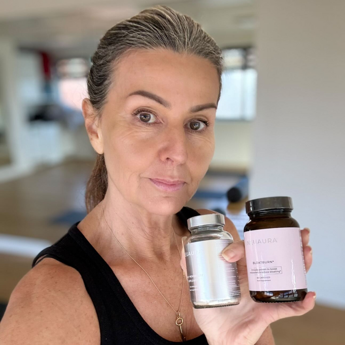 A person smiling and holding a bottle labeled 'Metabolic+' in a bright, well-lit room.