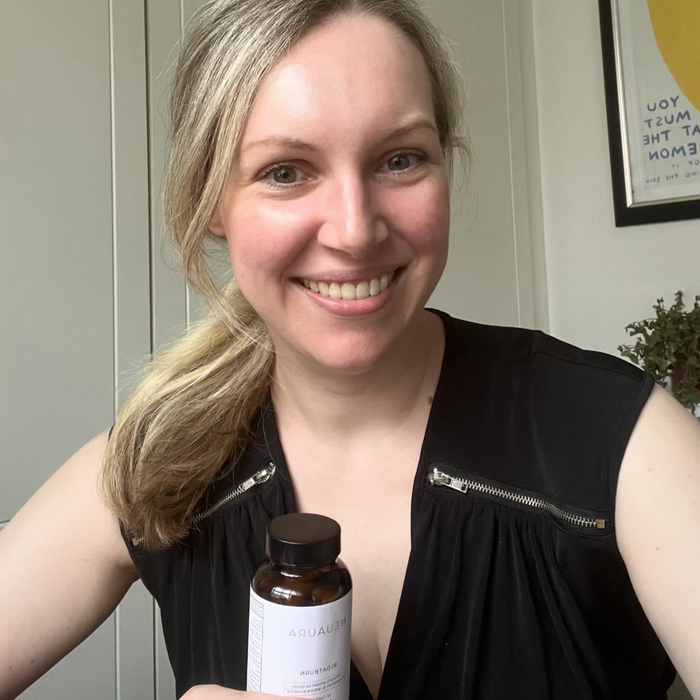 A person smiling and holding a bottle labeled 'Metabolic+' in a bright, well-lit room.
