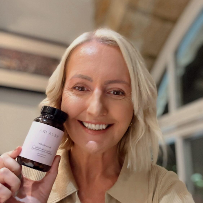 A person smiling and holding a bottle labeled 'Metabolic+' in a bright, well-lit room.